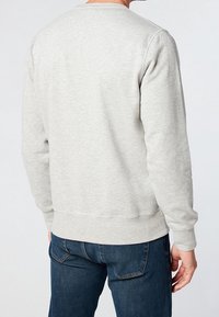 Sudadera gris de mangas largas y escote redondeado, con una tela simple y texturizada y dobladillo acanalado. Combinada con jeans azul.