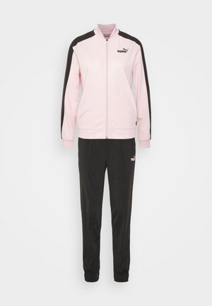 Różowa sportowa kurtka zapinana na zamek z czarnymi paskami na ramionach, zestawiona z czarnymi zwężanymi spodniami dresowymi, obie z logo Puma.