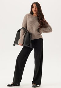 Maglione fluffy marrone chiaro, pantaloni neri a gamba larga, borsa nera con tracolla e slip-on neri con pois bianchi. Sfondo semplice.