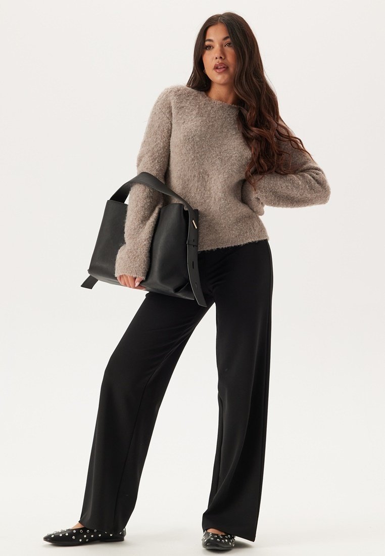 Maglione fluffy marrone chiaro, pantaloni neri a gamba larga, borsa nera con tracolla e slip-on neri con pois bianchi. Sfondo semplice.
