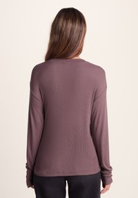 Long-sleeve shirt in muted mauve, ribbed texture, relaxed fit, scoop neck, and dropped shoulder seams. Minimalistic design, no visible logos.