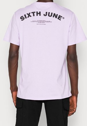 T-shirt en coton lilas à manches courtes, avec un logo incurvé "SIXTH JUNE" en texte noir gras au dos et des détails textuels supplémentaires.