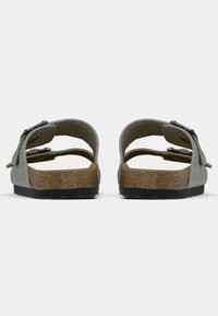 Γκρι σανδάλια με διπλές ρυθμιζόμενες λωρίδες, φελγούντα πέλματα και καουτσούκ σόλα. Σχεδίαση ανοιχτής πλάτης και λεία υφή στις λωρίδες.