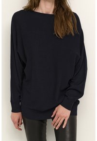 Navy blue oversized sweater with long sleeves, ribbed hem, and soft texture. Paired with slim black pants for contrast.