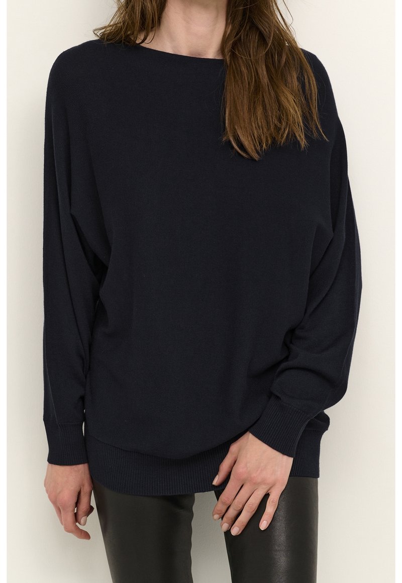 Navy blue oversized sweater with long sleeves, ribbed hem, and soft texture. Paired with slim black pants for contrast.