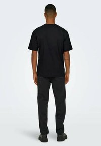 Camiseta negra de algodón con mangas cortas y cuello redondo, combinada con pantalones negros. Textura suave, diseño sencillo, sin logotipos ni patrones visibles.