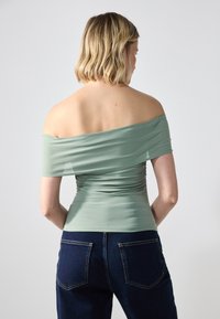 Top verde menta sin hombros con detalle fruncido, fabricado en una suave tela elástica, combinado con jeans de mezclilla oscura con bolsillos traseros.
