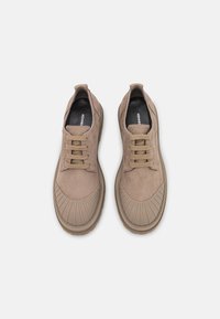 Scarpe in suede beige con lacci e suole in gomma rigate, caratterizzate da una punta tondeggiante e dettagli testurizzati vicino alla scatola delle dita.