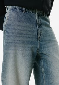 Svijetloplave traperice visokog struka, s izbljeđenim pranjem, vidljivim šavovima i ravnim nogavicama.