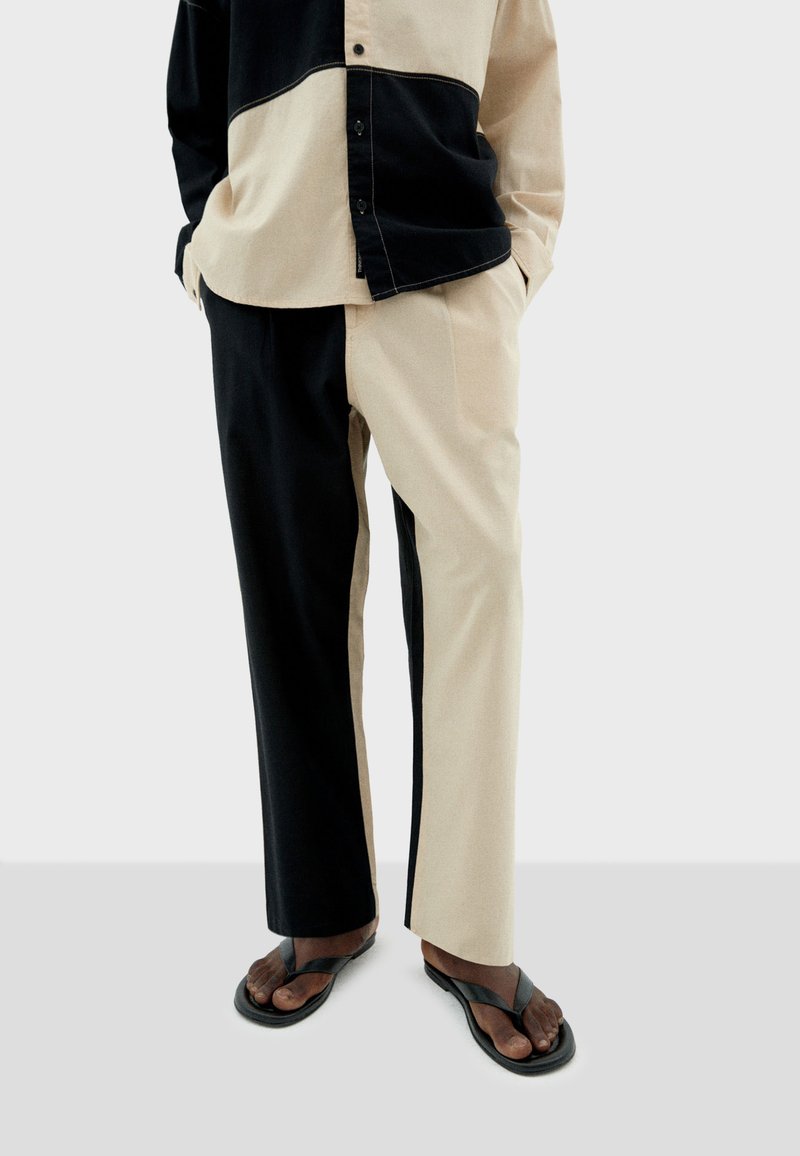 Conjunto de camisa y pantalones en tono dividido negro y beige, con un diseño de botón, textura de tela suave y combinado con sandalias negras de dedo.
