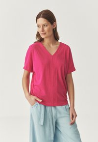 Korte mouw, V-hals top in felroze, gemaakt van zachte stof, met een relaxte pasvorm en subtiele naaddetails, gecombineerd met lichtblauwe broek.