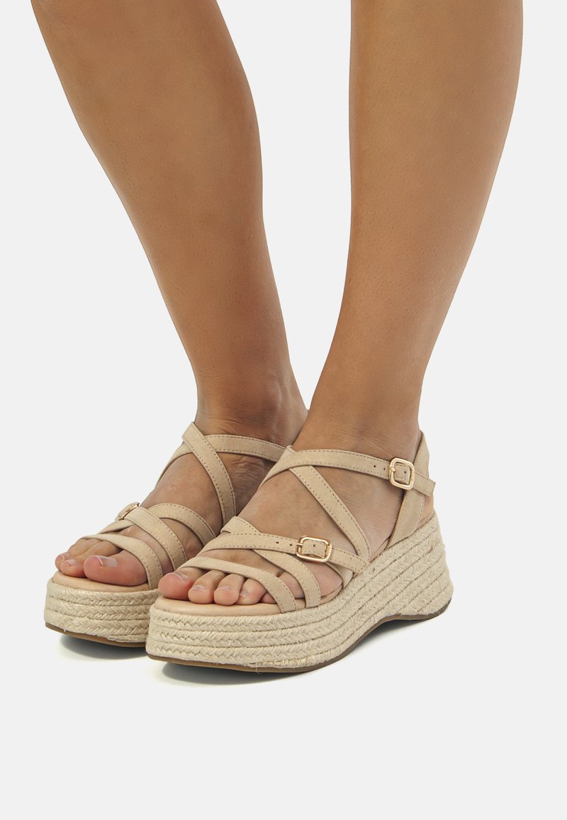 Sandale cu toc wedge bej, cu un design cu curea încrucișată, talpă din plută texturată și accente metalice. Potrivite pentru ținute casual.