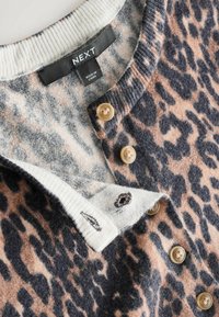 Gros plan d’un cardigan en laine à motif léopard avec des boutons beige et un col côtelé blanc marqué NEXT, fabriqué en Chine.
