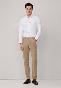 Chemise blanche boutonnée à boutons marron, associée à un pantalon chino beige et des chaussures marron foncé. Coupe slim avec col classique.