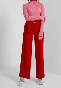 Röda vida byxor med bälte i midjan, i kombination med en rosa ribbad turtleneck. Tyget verkar mjukt och texturerat.