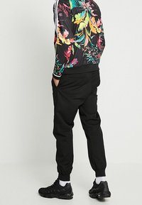 Svarta joggers med elastiska muddar, kombinerade med en blommig bomberjacka med livfulla färger och kontrasterande vita ränder på ärmarna.