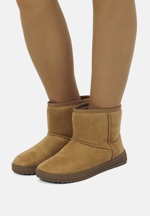 Bottines en suède beige avec un intérieur doux, bout rond et semelle en caoutchouc texturée. Comprend un simple revers et des détails de couture.