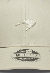Beige cap made of fabric with a stitched white logo, features a curved brim and adjustable strap, marked with a "9FIFTY" label.