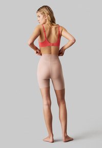 Red bra with adjustable straps and a clasp back, paired with nude high-waisted shaping shorts. Smooth texture, designed for support.