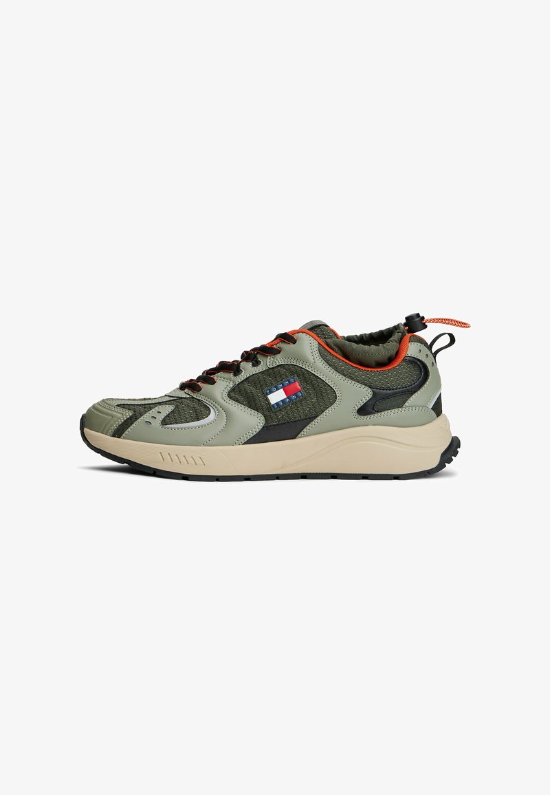 Baskets de sport en olive avec des accents noirs, présentant un upper texturé, des détails orange et une épaisse semelle beige.