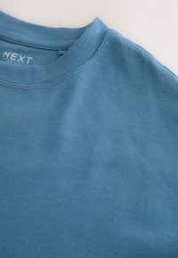 Tricou din bumbac bleu deschis, cu guler rotund cu nervuri, textură fină și fără modele sau accente vizibile. Eticheta mărcii este vizibilă în interiorul gâtului.