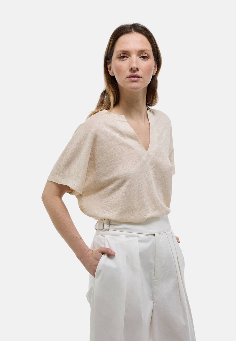 Haut en mélange de lin beige avec un col en V et des manches courtes, associé à un pantalon blanc taille haute avec des poches latérales et des plis.