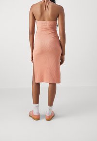 Robe midi côtelée sans bretelles de couleur pêche douce avec des fentes latérales. Associée à des chaussures roses et des chaussettes blanches avec des accents de couleur.