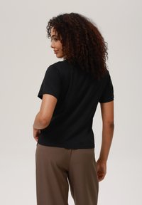 Sort kortærmet t-shirt med rund halsudskæring, glat tekstur og tætsiddende design, parret med brune bukser.
