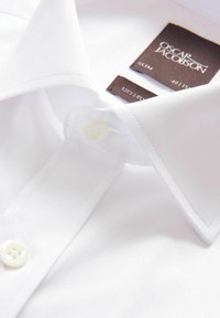 Vit skjorta med smal passform i mjukt tyg, med klassiskt krage, enkel knappstängning och etiketter med märke- och tygdetaljer.