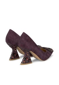 Pump in suede viola con accentuazione di gioielli sul tacco. Design unico del tacco triangolare con gemme decorative in tonalità di rosso e viola.
