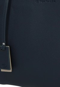 Borsa a mano in pelle blu navy texturizzata con un piccolo tag, finitura morbida e una forma strutturata adatta all'uso quotidiano.
