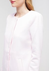 Ljust rosa, texturerad kavaj med rund halslinje, fram zip-stängning och sidofickor, designad med en figurnära silhuett.