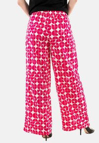 Pantaloni ampi rosa e crema con un motivo geometrico. Presentano una vita arricciata e una texture liscia, indossati con tacchi alti neri.