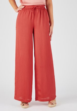 Pantaloni a gamba larga in un colore ruggine chiaro, realizzati in tessuto texturizzato con un design plissettato, dotati di una vita elasticizzata e di un cordoncino.