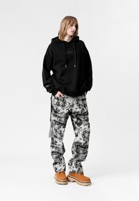 Sudadera negra de gran tamaño con un bolsillo frontal, combinada con pantalones de patrón blanco y negro y botas gruesas marrones. Tejidos texturizados y diseño casual.