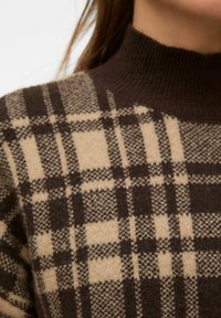 Sweter dziany z wysokim kołnierzem w brązowo-beżową kratę z różnorodnymi teksturami i odcieniami na materiale.