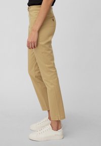 Pantalons en coton beige à jambes droites, dotés de poches avant et arrière, et de détails de couture subtils ; portés avec des baskets blanches.