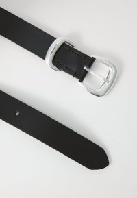 Svart läderbälte med silverfärgad spänne och Calvin Klein-logotyp på slingan, lagt platt på en vit yta.