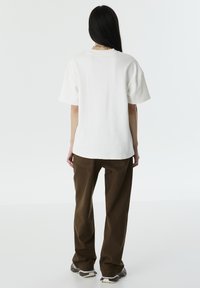 Witte katoenen t-shirt met korte mouwen, losse pasvorm, gecombineerd met bruine wijde broek en zwarte sneakers. Eenvoudig, minimalistisch ontwerp.