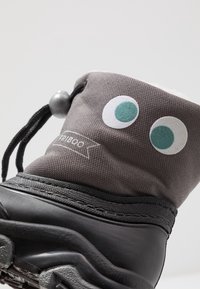 Botte en tissu gris avec de grands yeux mobiles blancs et turquoise. Dessus en caoutchouc noir et fermeture réglable par cordon. Doublure intérieure douce.