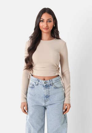 Top corto de punto beige con mangas largas, que cuenta con cordones laterales para ajuste, combinado con jeans baggy de lavado claro.