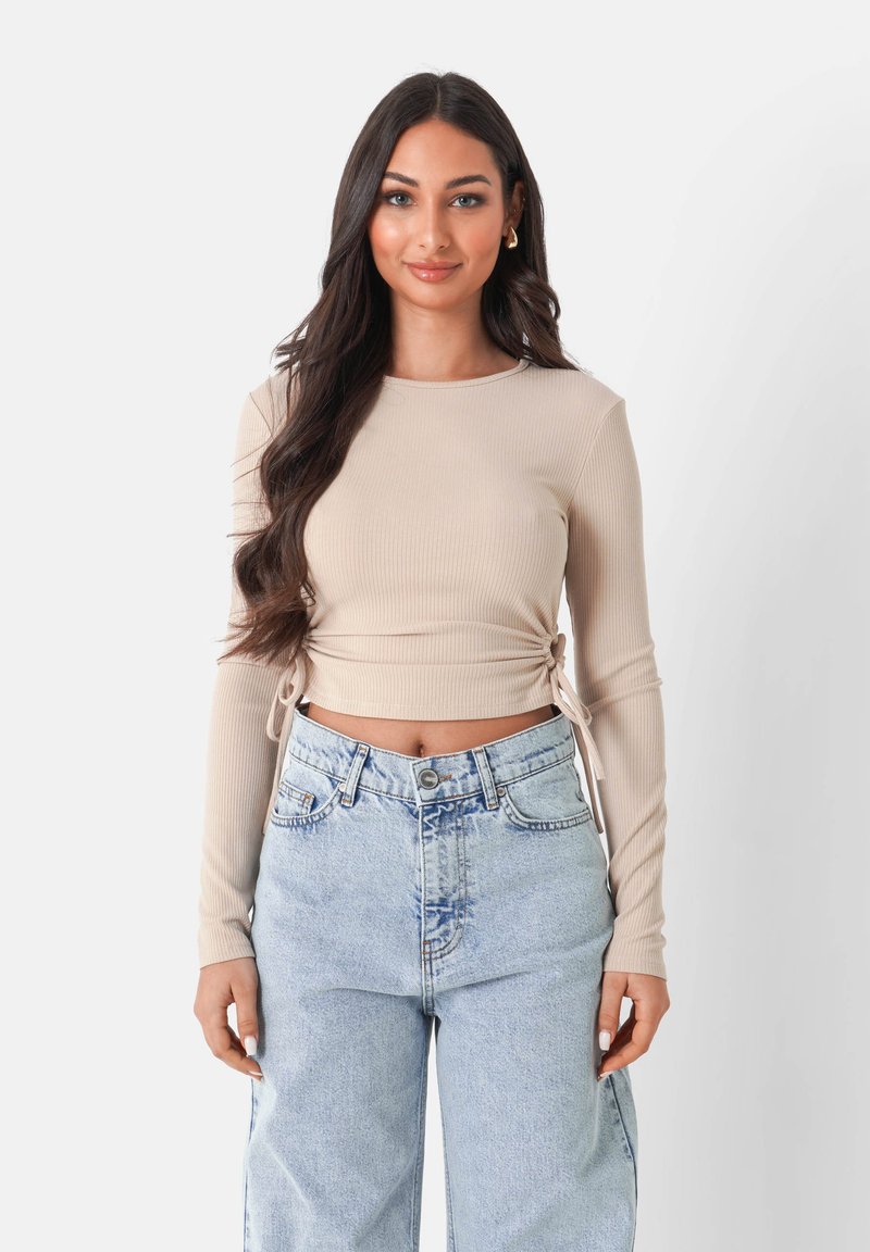 Beżowy prążkowany crop top z długimi rękawami, z bocznymi sznurkami do regulacji, połączony z jasnoniebieskimi luźnymi dżinsami.