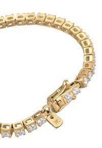 Goldfarbener Metallarmreif mit quadratischen Gliedern, eingebetteten klaren Edelsteinen und einem sicheren Verschluss mit einem kleinen Anhänger. Glatte Textur und polierte Oberfläche.