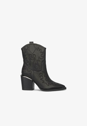 Bottes noires en cuir jusqu'à la cheville avec un bout pointu, des coutures détaillées et un talon épais en bloc avec un accent argenté sur le côté.