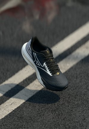 Black and white running shoe mid-air above asphalt with white lane markings, small particles of dirt kicked up beneath the shoe.