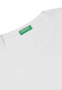 Bílá bavlněná tričko s kulatým žebrovaným výstřihem. Obsahuje zelenou visačku s nápisem "UNITED COLORS OF BENETTON" poblíž límečku.