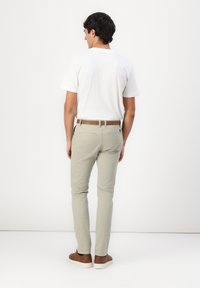 Pantaloni grigi chiari in cotone, con una vestibilità slim e passanti per la cintura, abbinati a una maglietta bianca e scarpe casual marroni.
