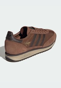 Brown suede and leather sneaker with three dark brown stripes, textured ankle collar, gold branding, and a light-colored rubber sole.