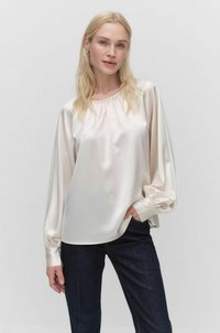 Silkkinen kerma collegepaita, jossa on kerätty pääntie ja puffatut pitkät hihat. Yhdistetty tummiin farkkuihin. Tasaisen sileä rakenne ja pehmeä kiilto.