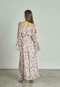 Schulterfreies, blumiges Maxikleid mit Rüschensäumen, das eine Mischung aus lila und rosa Blumen auf einem hellen Hintergrund präsentiert. Dünner Taillengürtel.